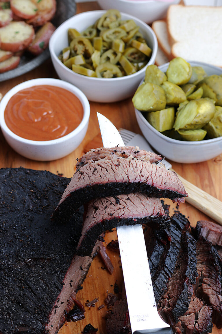 cooked smoked brisket, slice laying over knife, served with condiments