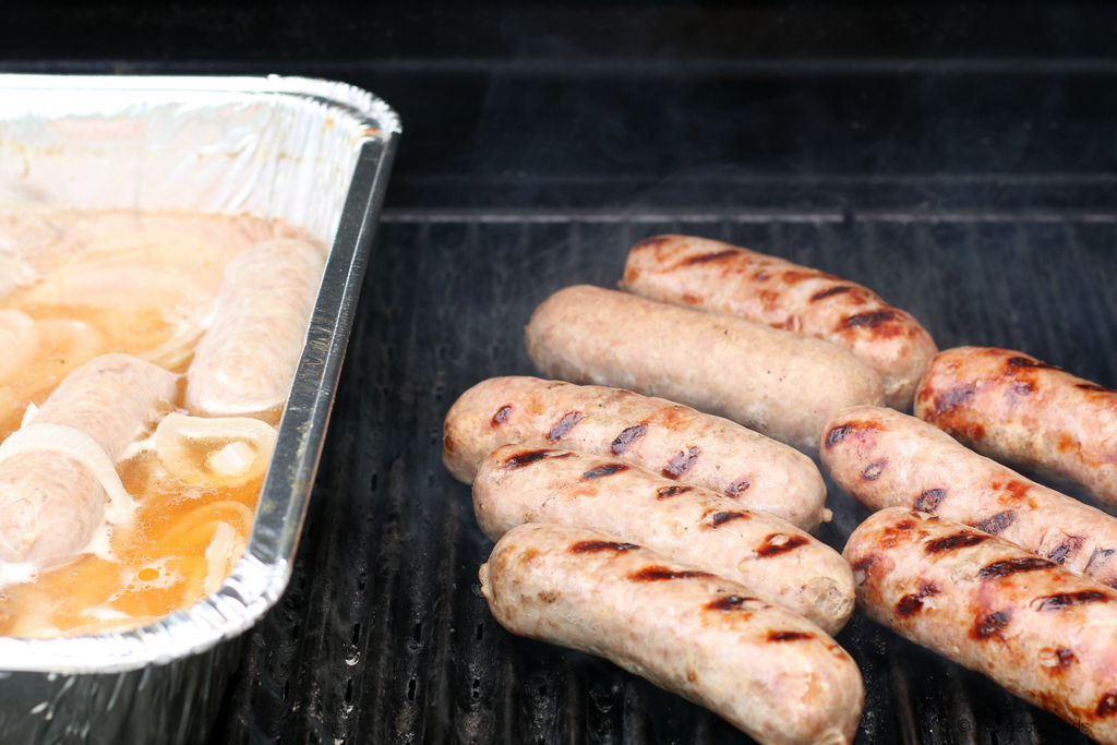 eight brats being grilled, along with beer and onions