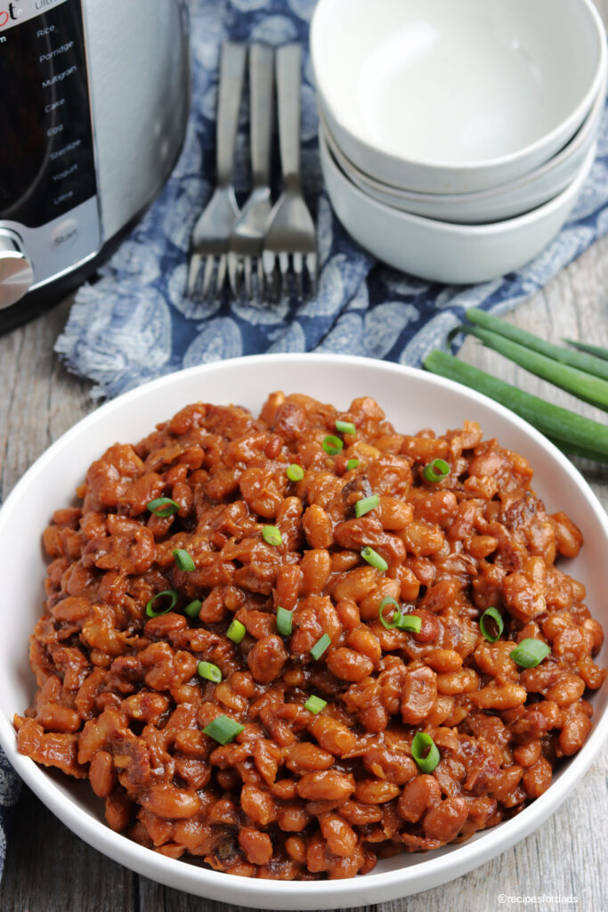 bbq baked beans served in white bowl with pressure cooker in the background