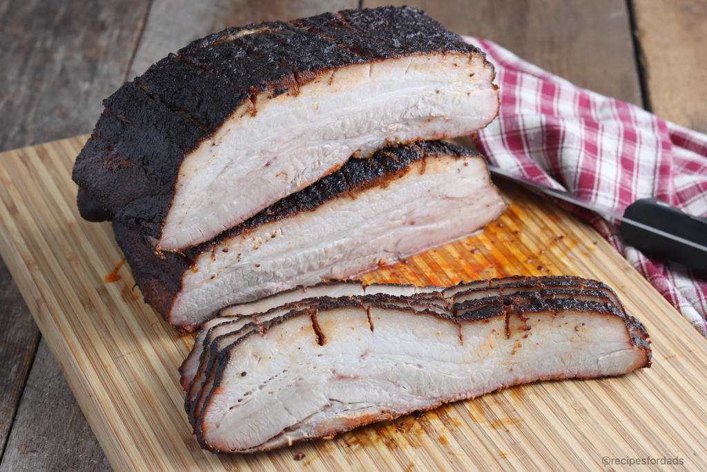 Smoked Pork Belly sliced on a cutting board with red and white checked napkin