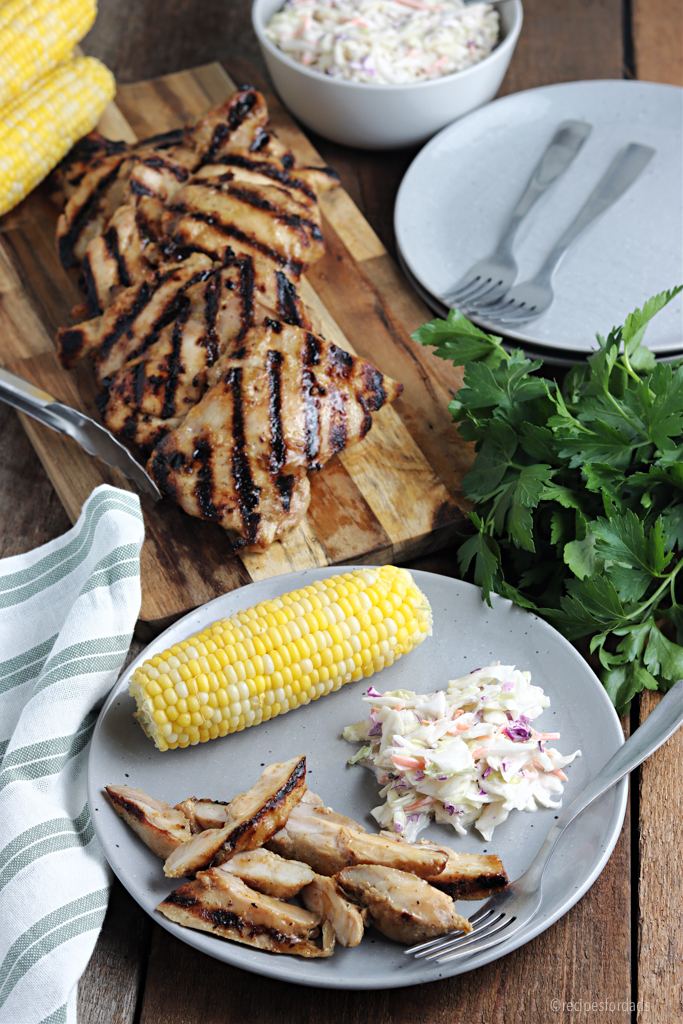Grilled chicken thighs with cole slaw and corn.