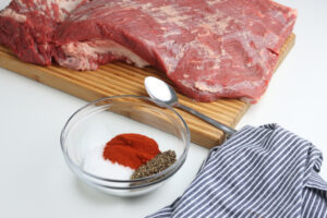 beef brisket on cutting board with spices in clear glass bowl