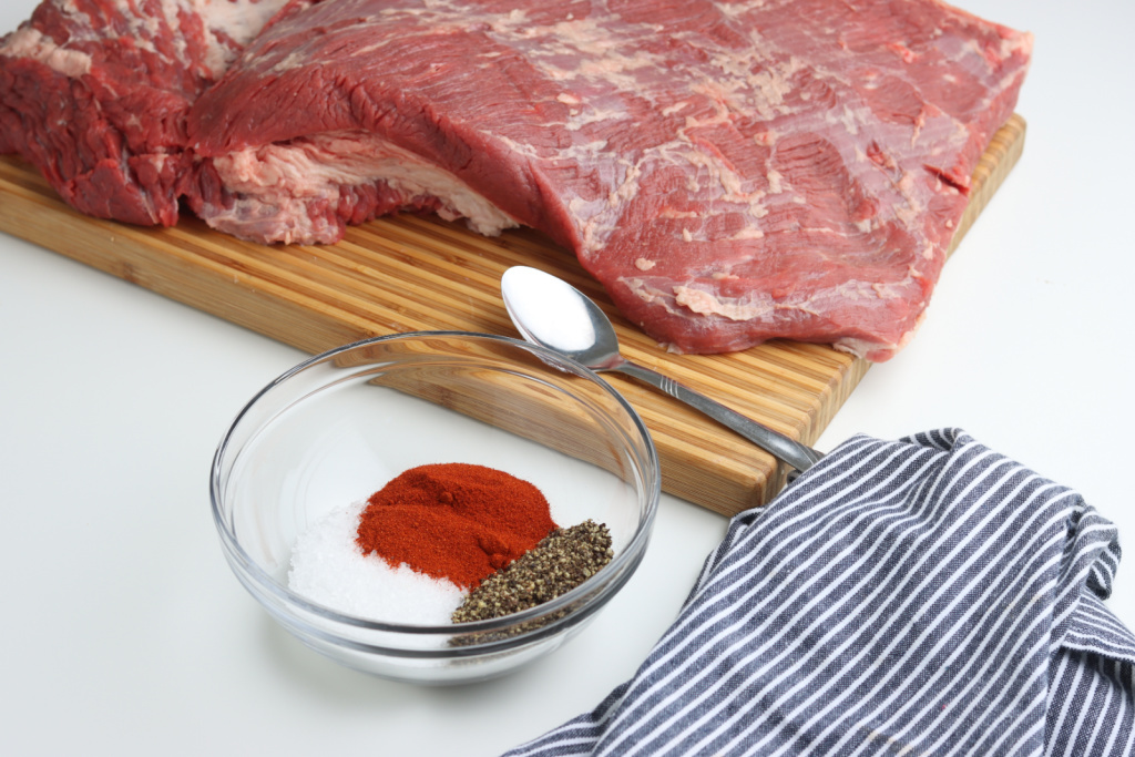 beef brisket on cutting board with spices in clear glass bowl