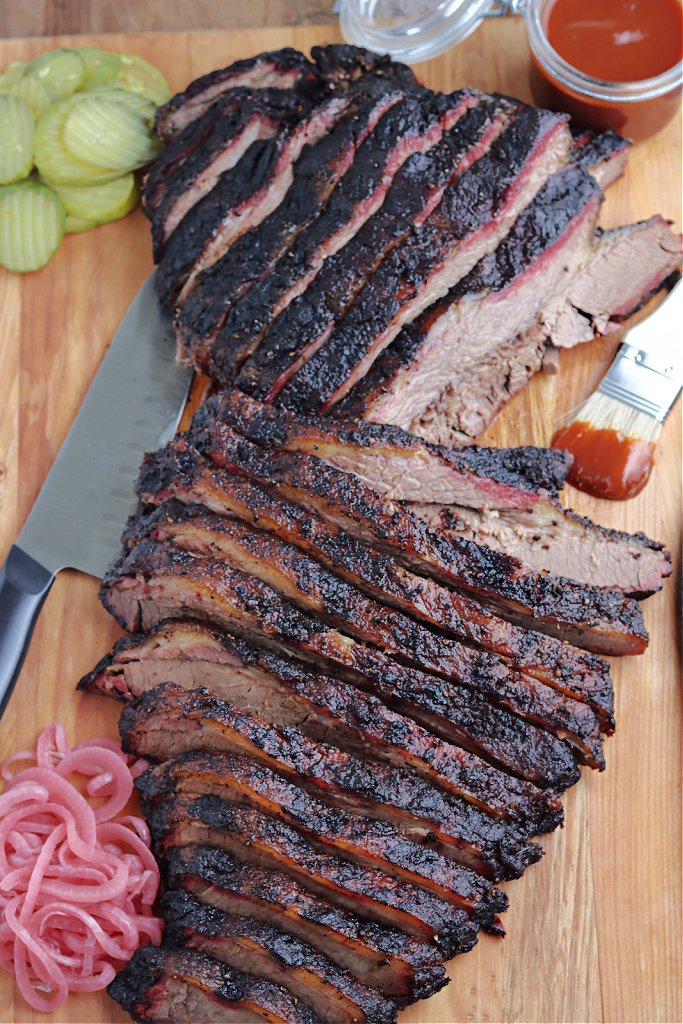 smoked brisket sliced on cutting board with barbecue sauce