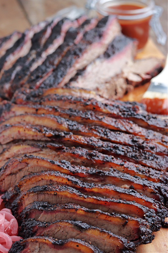 smoked brisket sliced on cutting board with barbecue sauce