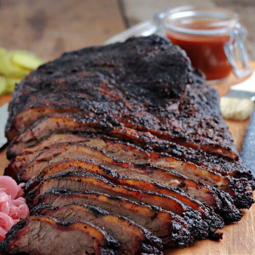 smoked brisket sliced on cutting board with barbecue sauce