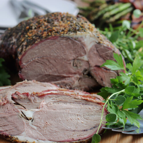 smoked leg of lamb serve on wood board with fresh herbs