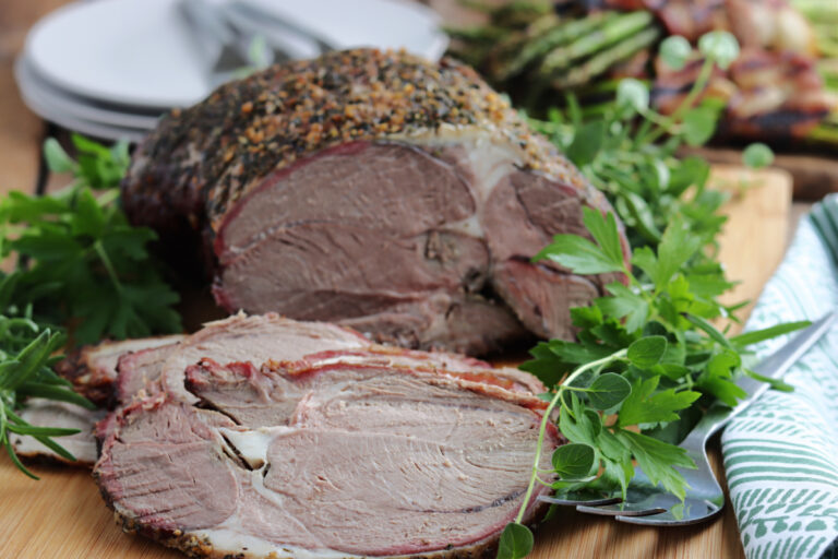 smoked leg of lamb serve on wood board with fresh herbs