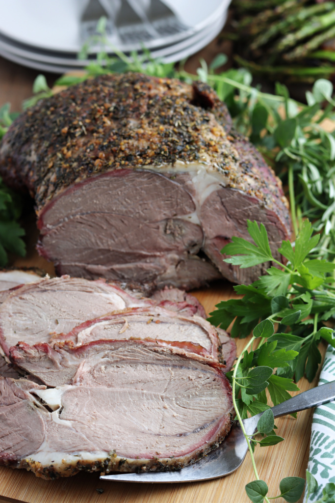 smoked leg of lamb serve on wood board with fresh herbs