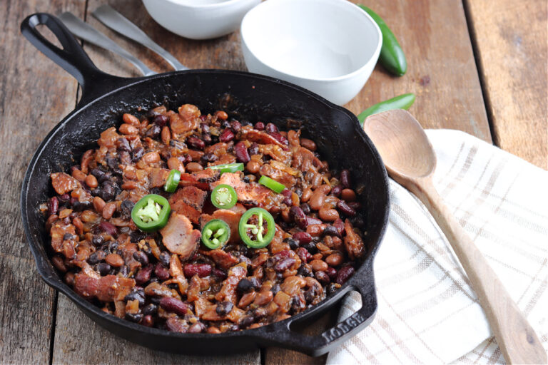 smoked baked beans in cast iron skillet with wooden spoon for serving